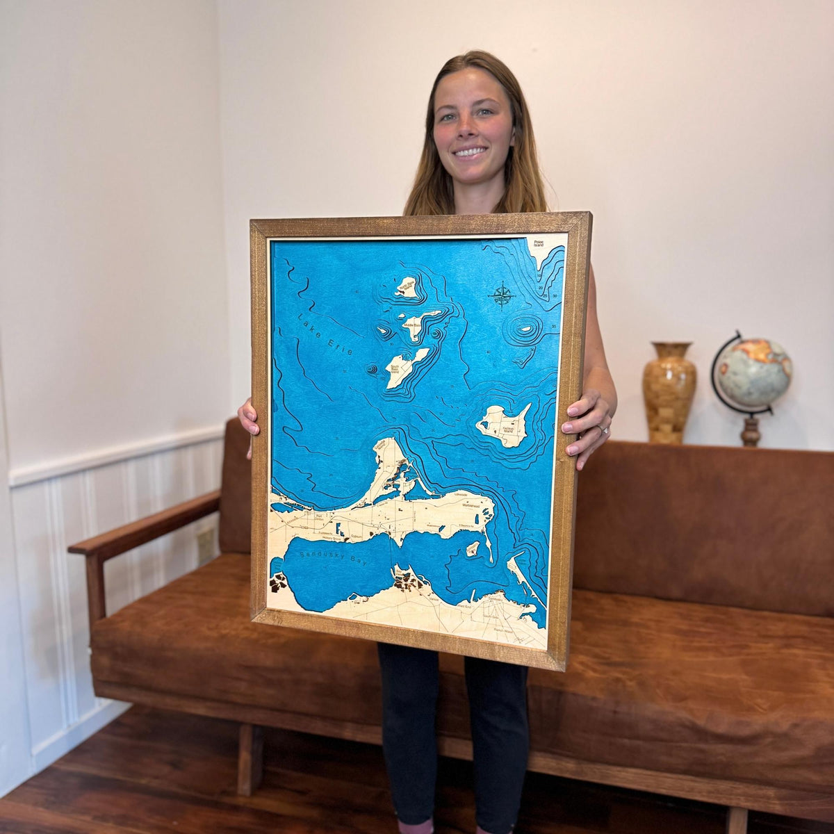 Woman holding a map of a Lake Erie Islands map with a couch and decorative items in the background.