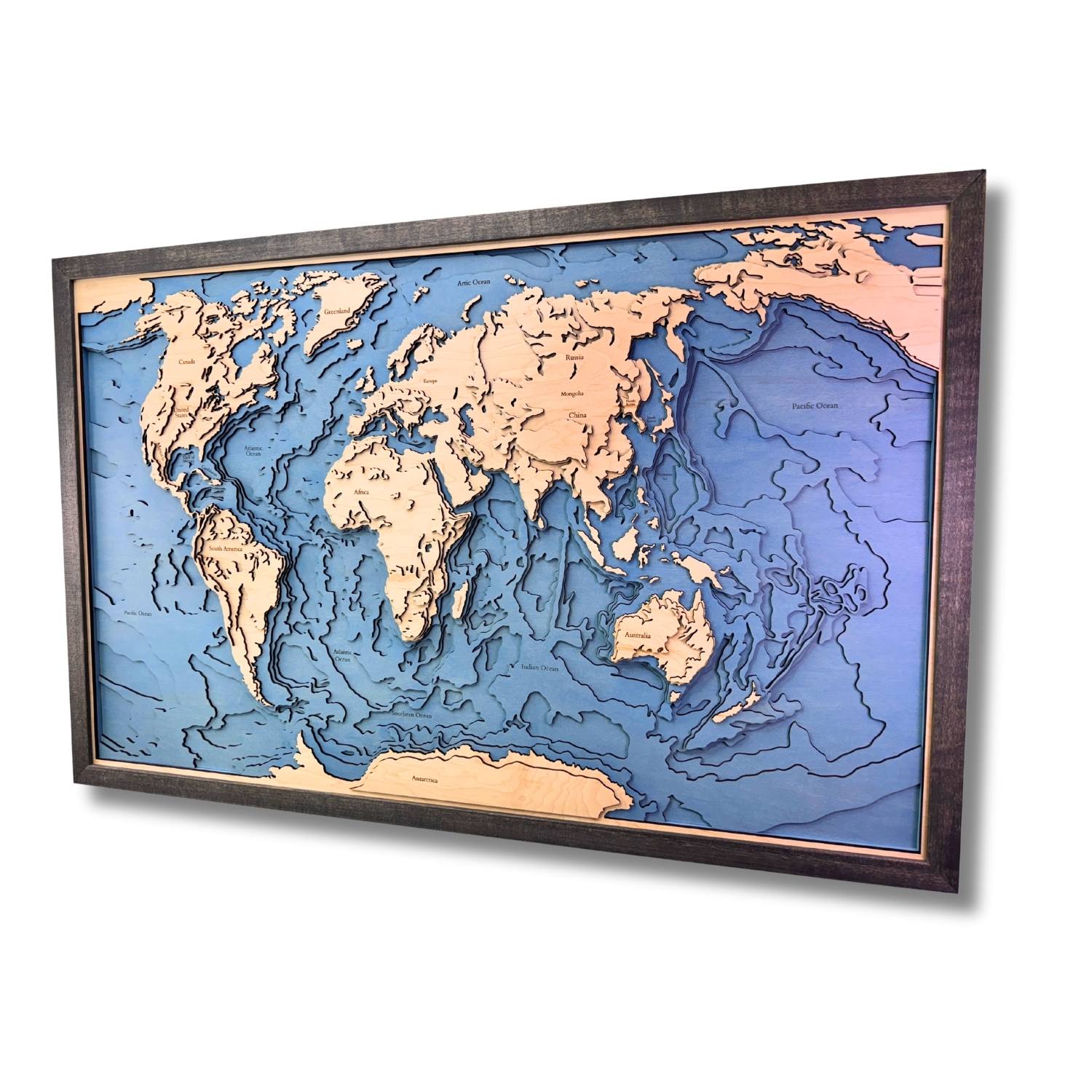 Sideview of a world map with raised topographic features in a wooden frame on a white background.