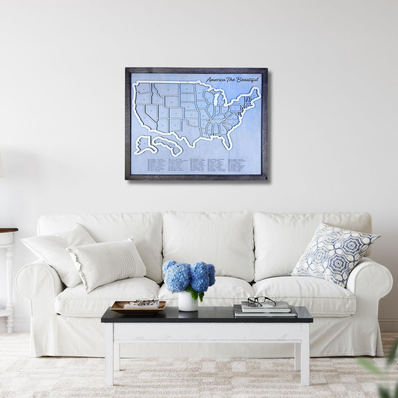 Wooden United States Travel Map hanging on a wall in a living room above a sofa and coffee table. 