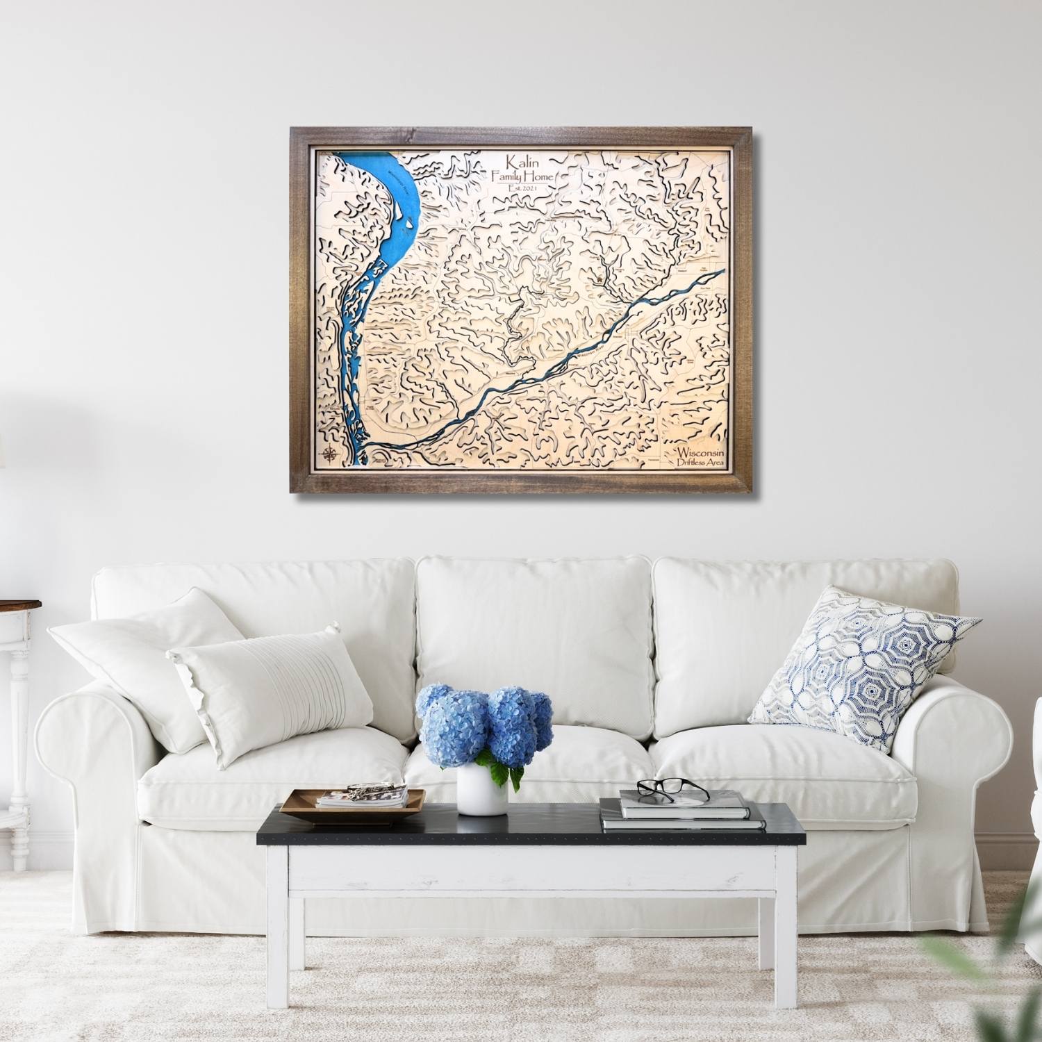 Framed topographic map above a white sofa with decorative pillows and a coffee table.