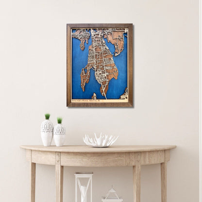 Framed wooden map of Bristol, RI hanging on wall above a wooden table with decorative items. 