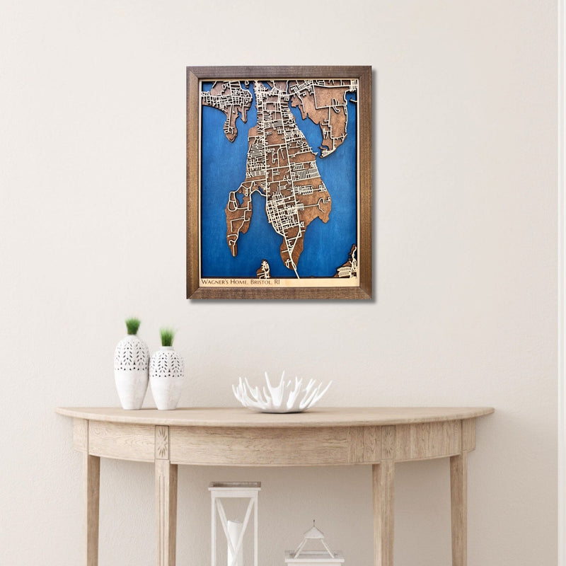 Framed wooden map of Bristol, RI hanging on wall above a wooden table with decorative items. 