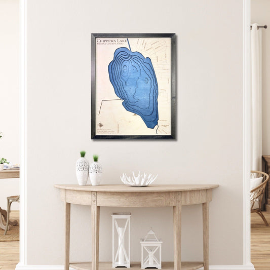 Framed 3D wooden map of Chippewa Lake on a wall above a wooden table.