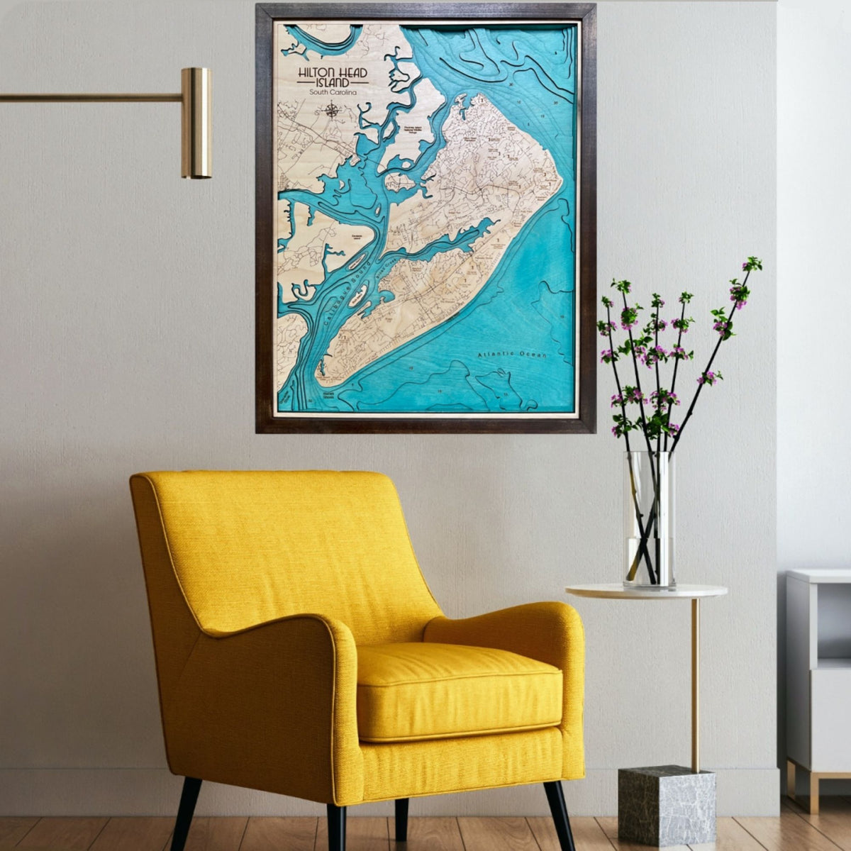 Large multi water layer map of Hilton Head hanging on a wall above a yellow chair. 