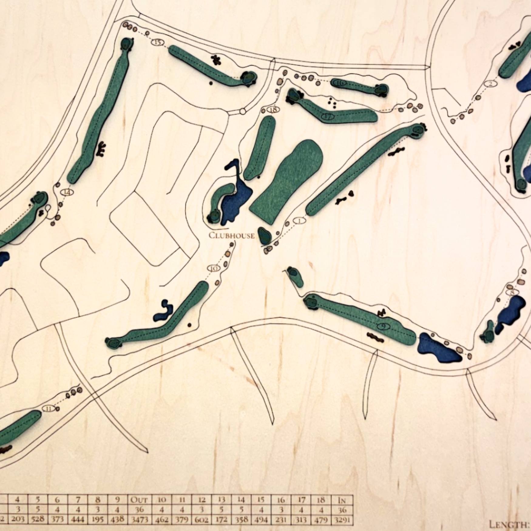 Close up of wooden golf course map with green fairways, blue water hazards, and engraved text. 