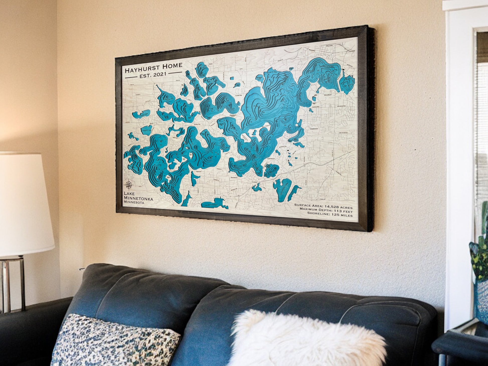 Custom wooden map of Lake Minnetonka hanging on wall above a couch. 