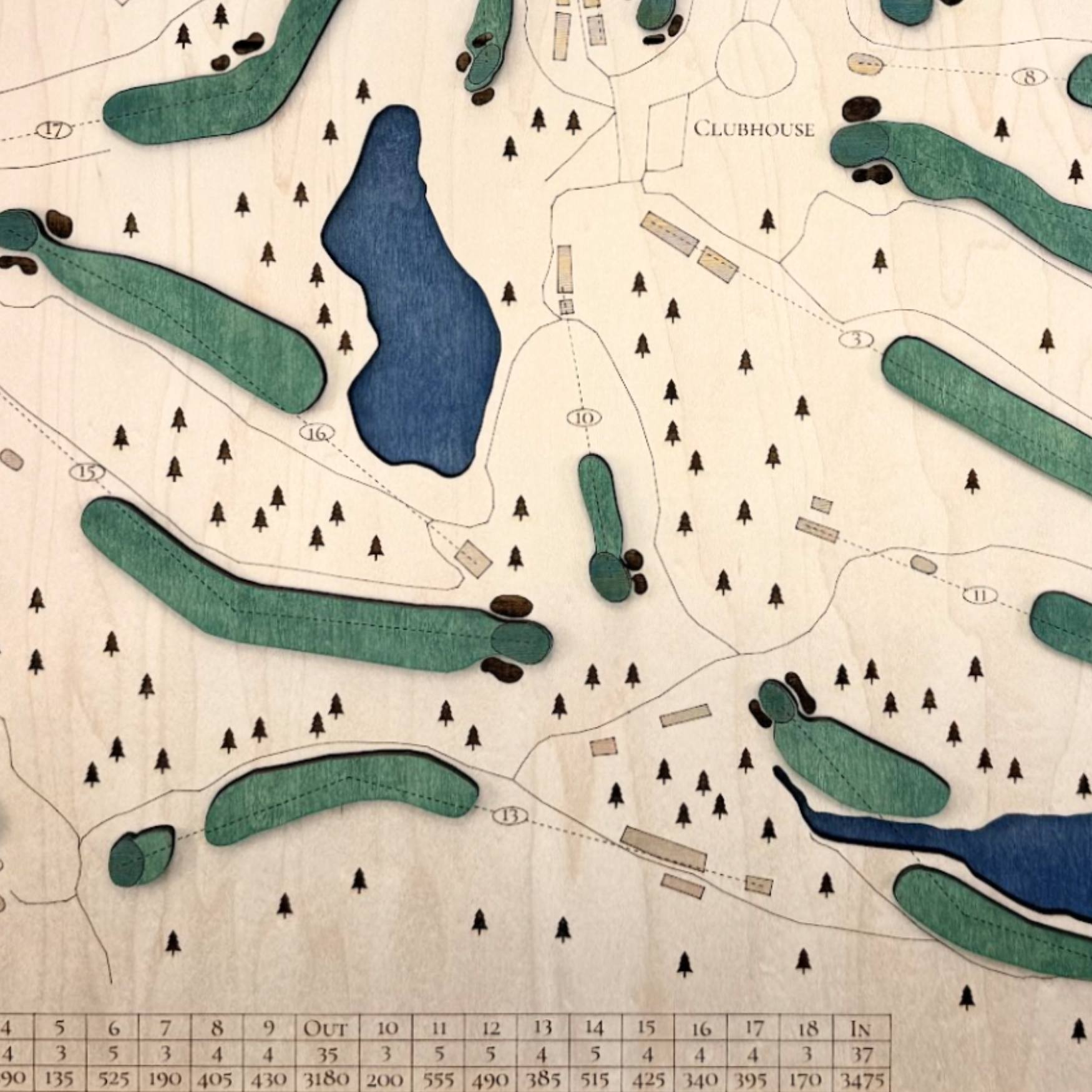 Close up of wooden golf course map with green fairways, blue water hazards, and engraved text. 
