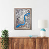 Framed wooden Philadelphia city map on a wall above a wooden console table with a lamp and plant.