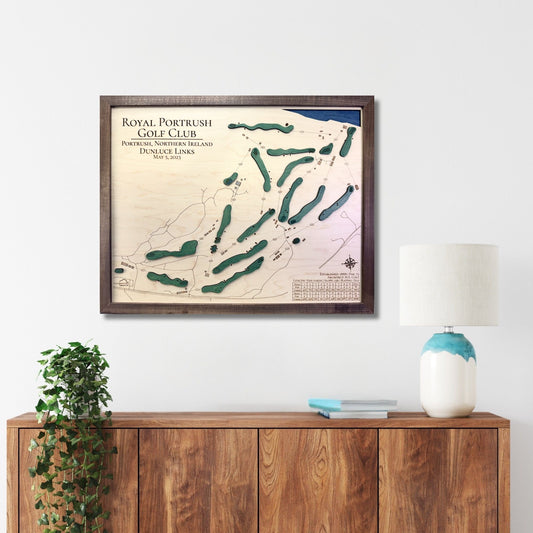 Framed map of Royal Portrush Golf Club on a wall above a wooden cabinet.
