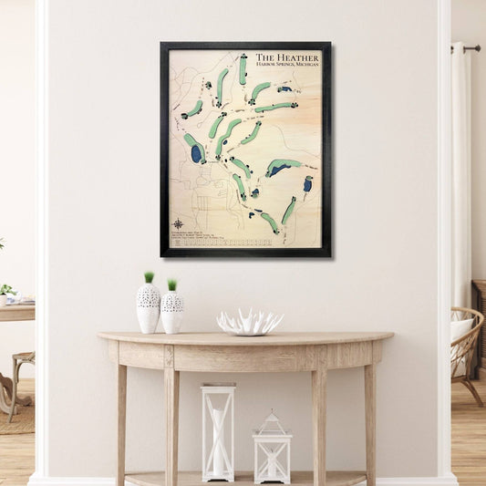 Framed wooden golf map of The Heather golf course on a wall above a wooden table.