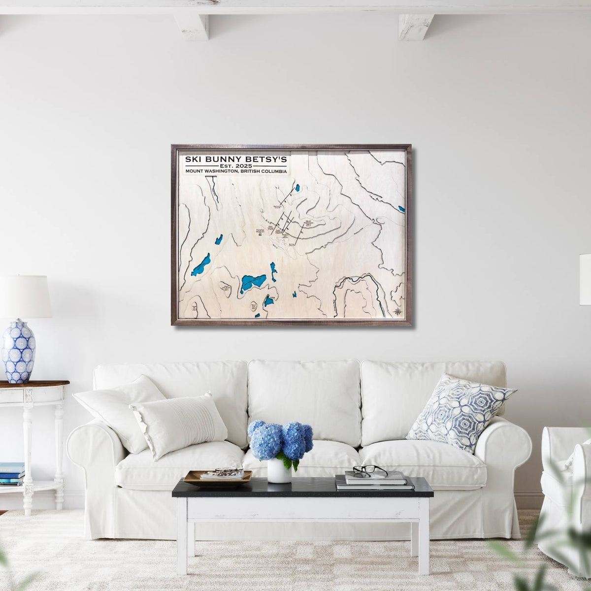 Framed wooden topographic map on a wall above a white sofa in a living room.