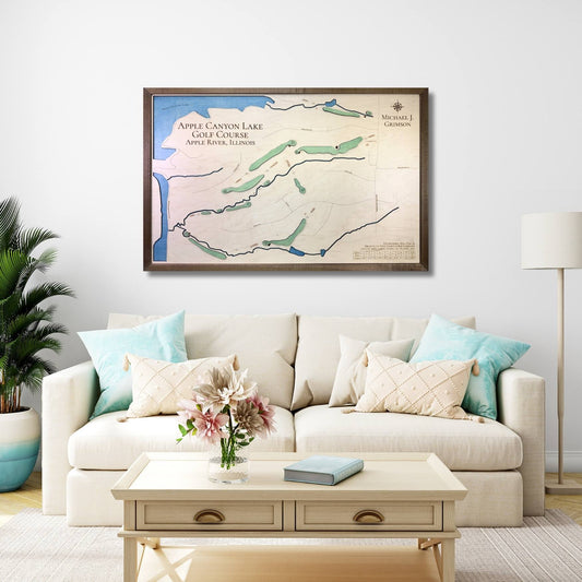 Living room with a framed wooden map of Apple Canyon Lake Golf Course on the wall above a beige sofa with decorative pillows.