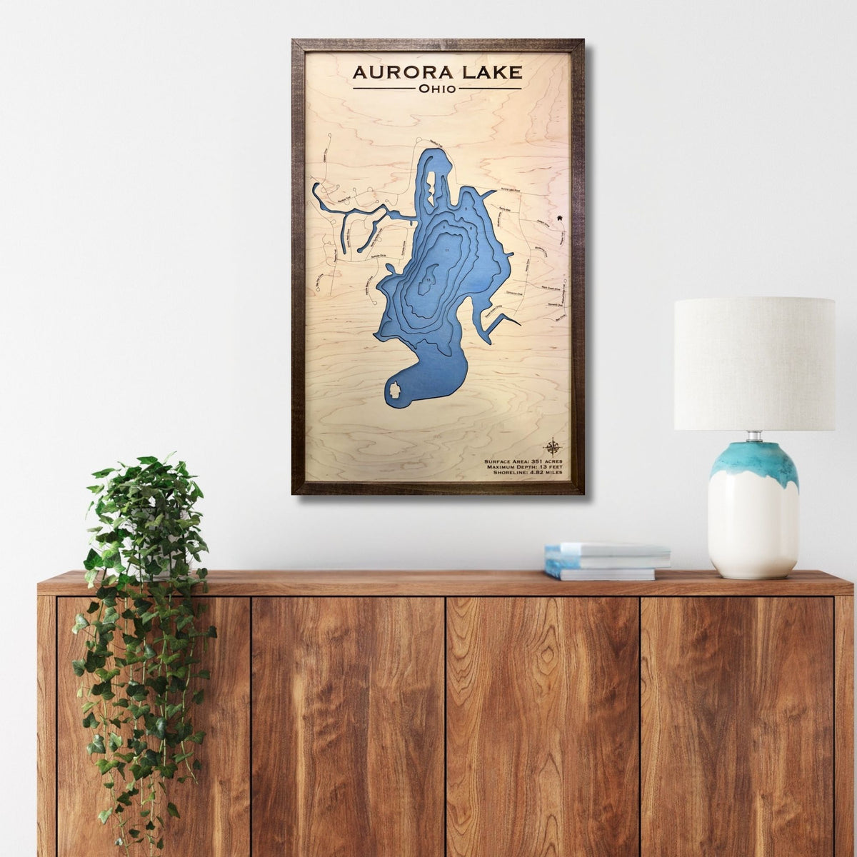 Wooden wall art of Aurora Lake, Ohio on a white wall above a wooden cabinet.