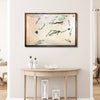 Framed wooden golf course map on a wall above a wooden table with decorative items.