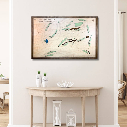 Framed wooden golf course map on a wall above a wooden table with decorative items.