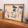 Framed 3D map of Catawba Island Club on a wooden surface with decorative items.