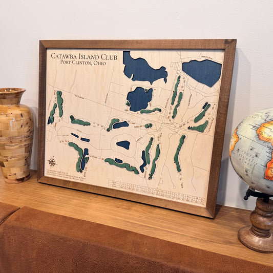 Framed 3D map of Catawba Island Club on a wooden surface with decorative items.
