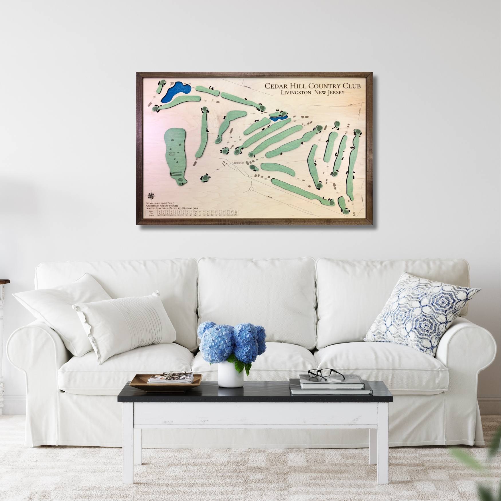 Framed wooden golf course map above a white sofa in a living room.