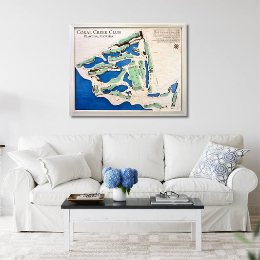 Framed wooden golf map of Coral Creek Club on a wall above a white sofa with decorative pillows.