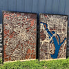 Two large city maps sitting outside in the grass and propped against a stone wall. 