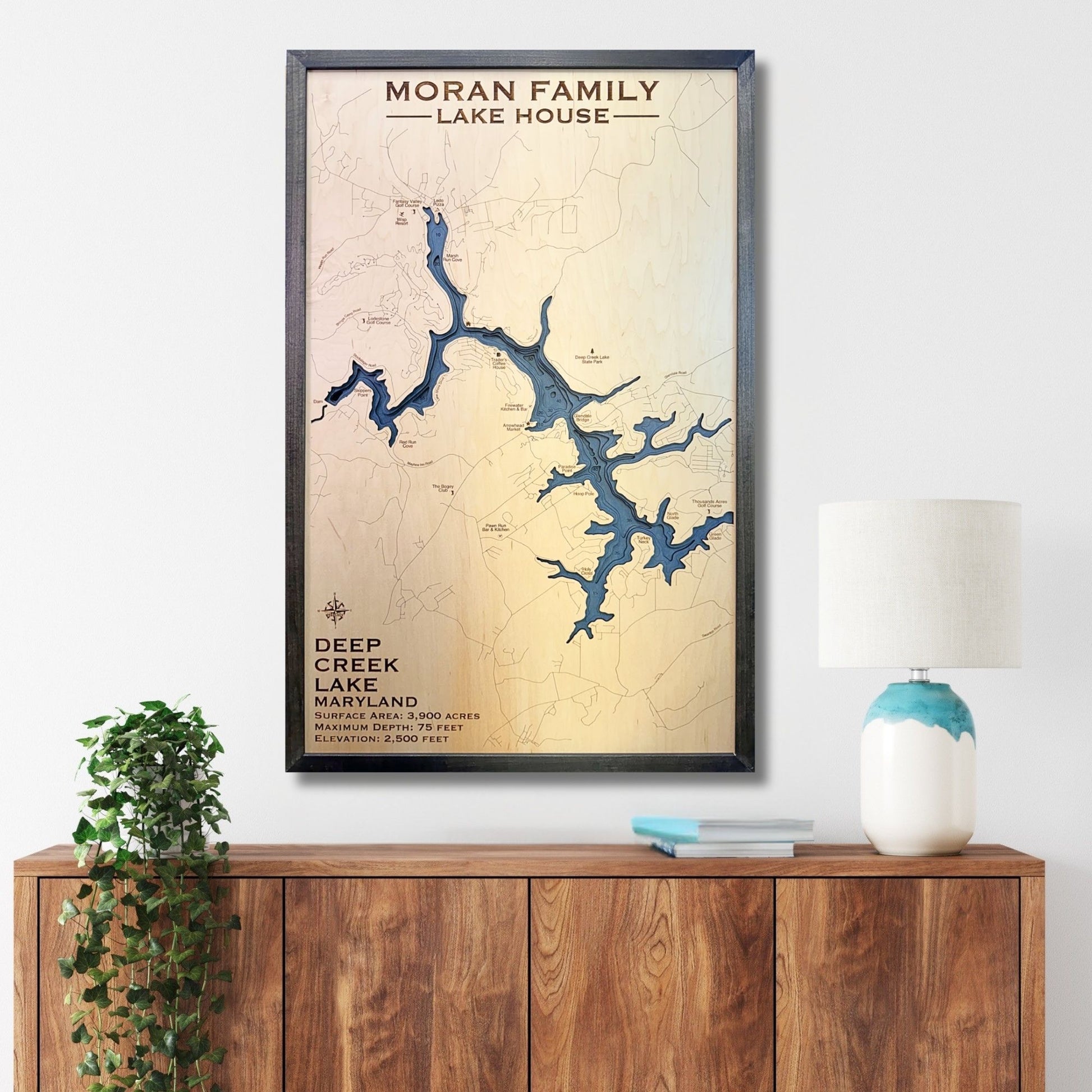 Custom wooden map of Deep Creek Lake on a wall above a wooden cabinet with decor items.