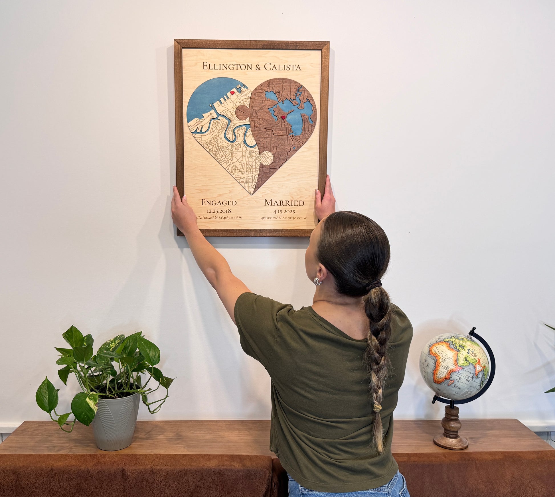 A woman is hanging the two-toned (yin yang) heart-shaped map on a wall above a dresser. 