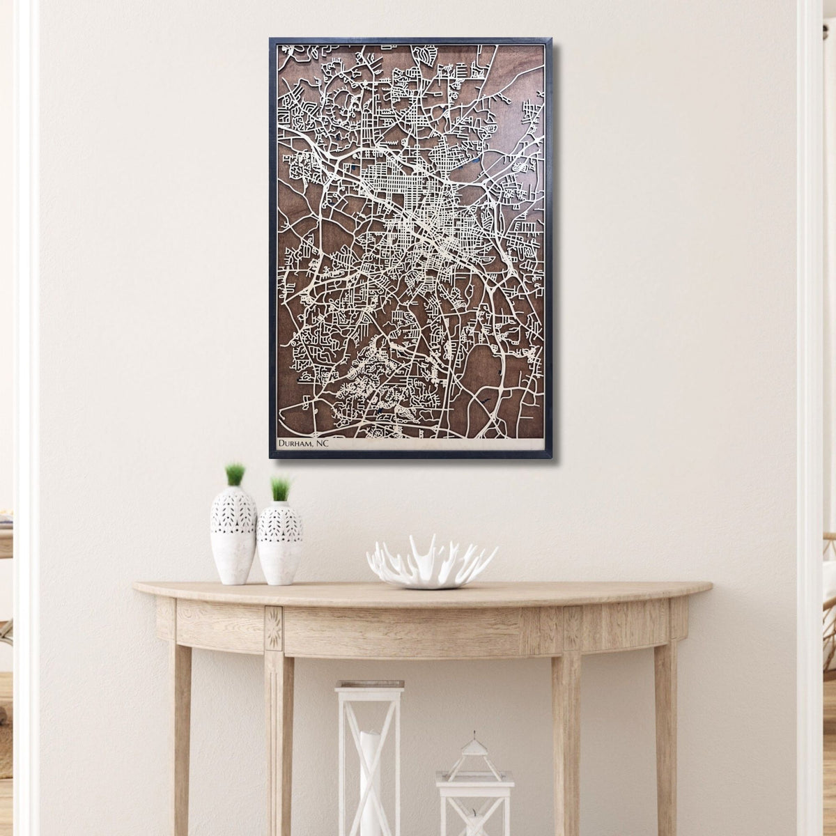 Wooden map of Durham, NC hanging on a wall above a wooden table containing decorative items. 