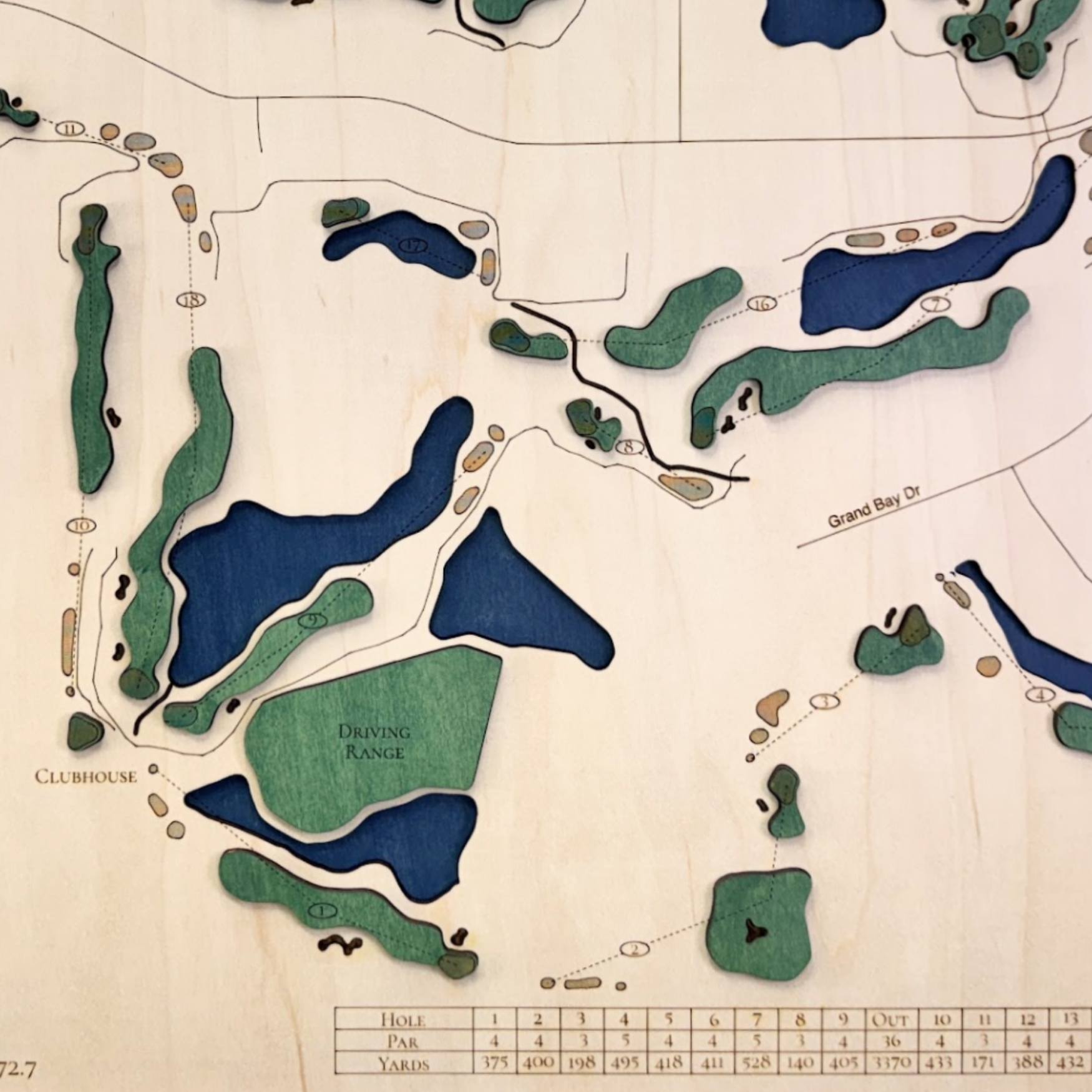 Close up of wooden golf course map with green fairways, blue water hazards, and engraved text. 