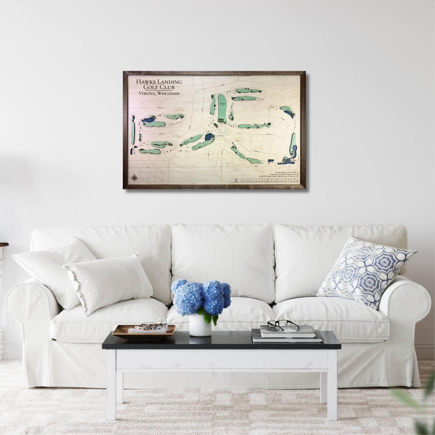 Living room with a white sofa, coffee table, and framed wooden golf map on the wall.