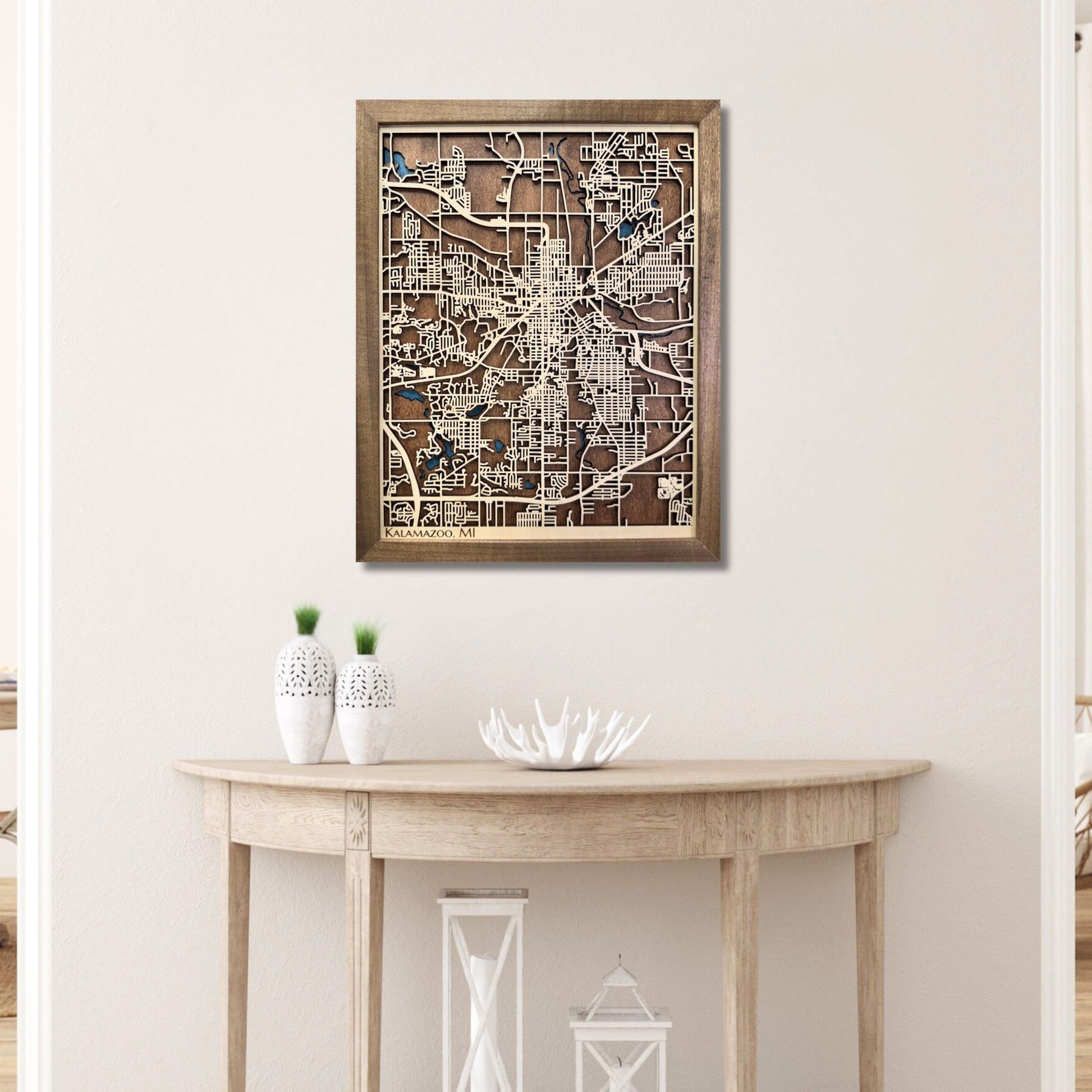 Framed wooden Kalamazoo city map on a wall above a wooden console table.