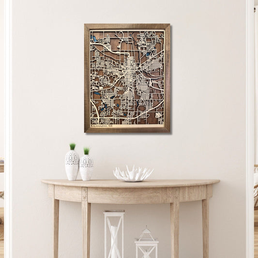Framed wooden Kalamazoo city map on a wall above a wooden console table.