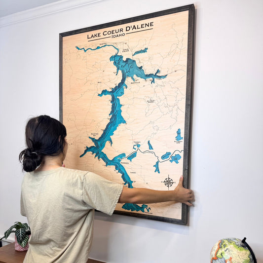 Person hanging a framed map of Lake Coeur d'Alene on a wall