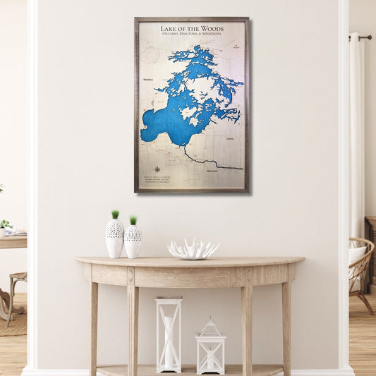 Framed wooden map of Lake of the Woods on a wall above a wooden table.