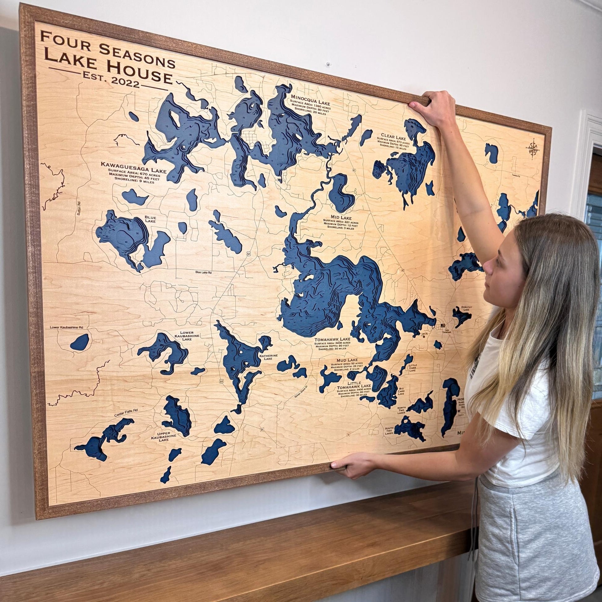 Woman hanging a large custom map that has many different lakes on it. 