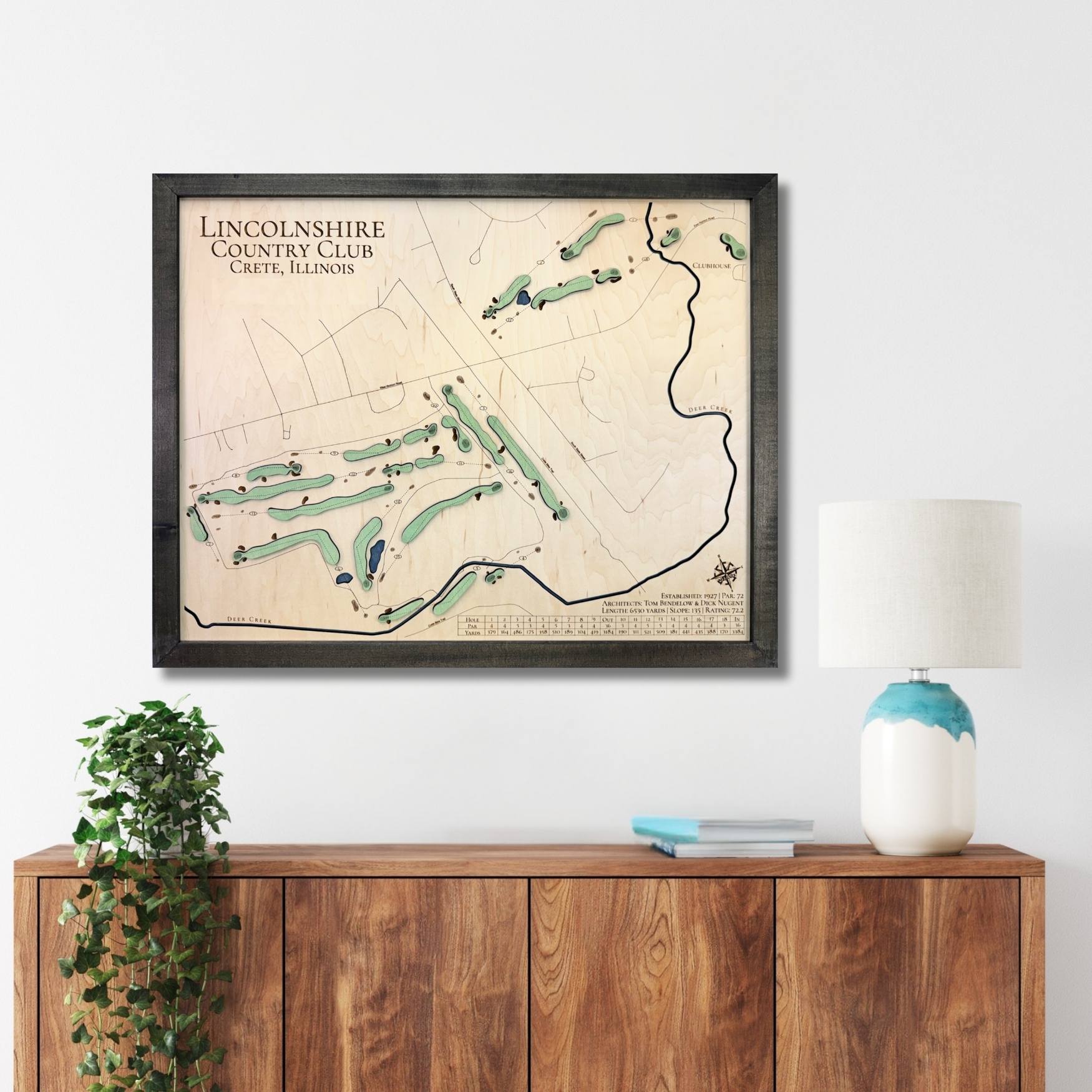 Framed wooden golf map of Lincolnshire Country Club on a wall above a wooden console table.