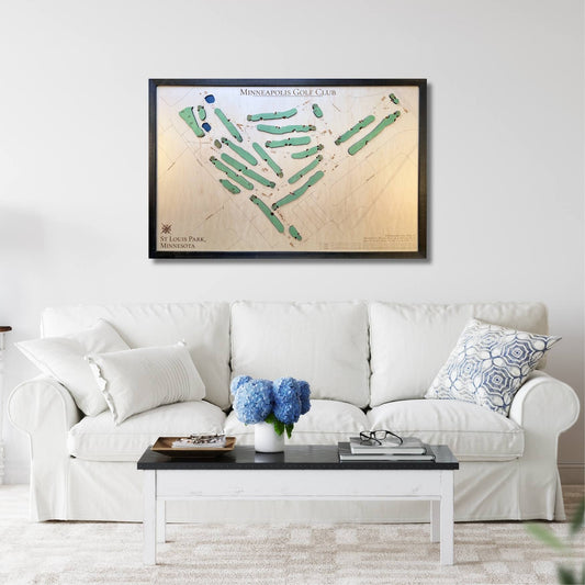 Framed golf course map on a wall above a white sofa with decorative pillows.