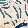 Close up of wooden golf course map with green fairways, blue water hazards, and engraved text. 