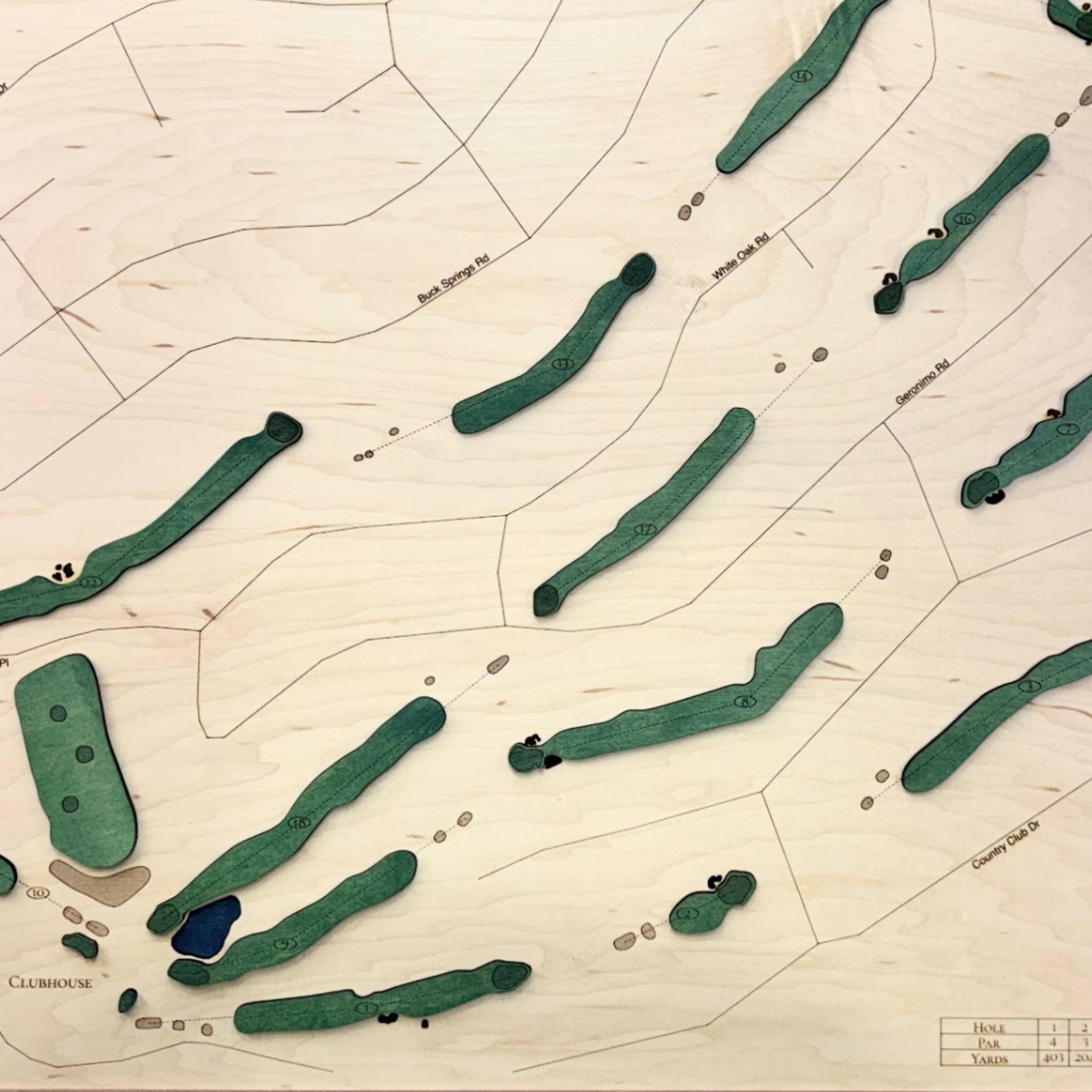 Close up of wooden golf course map with green fairways, blue water hazards, and engraved text. 