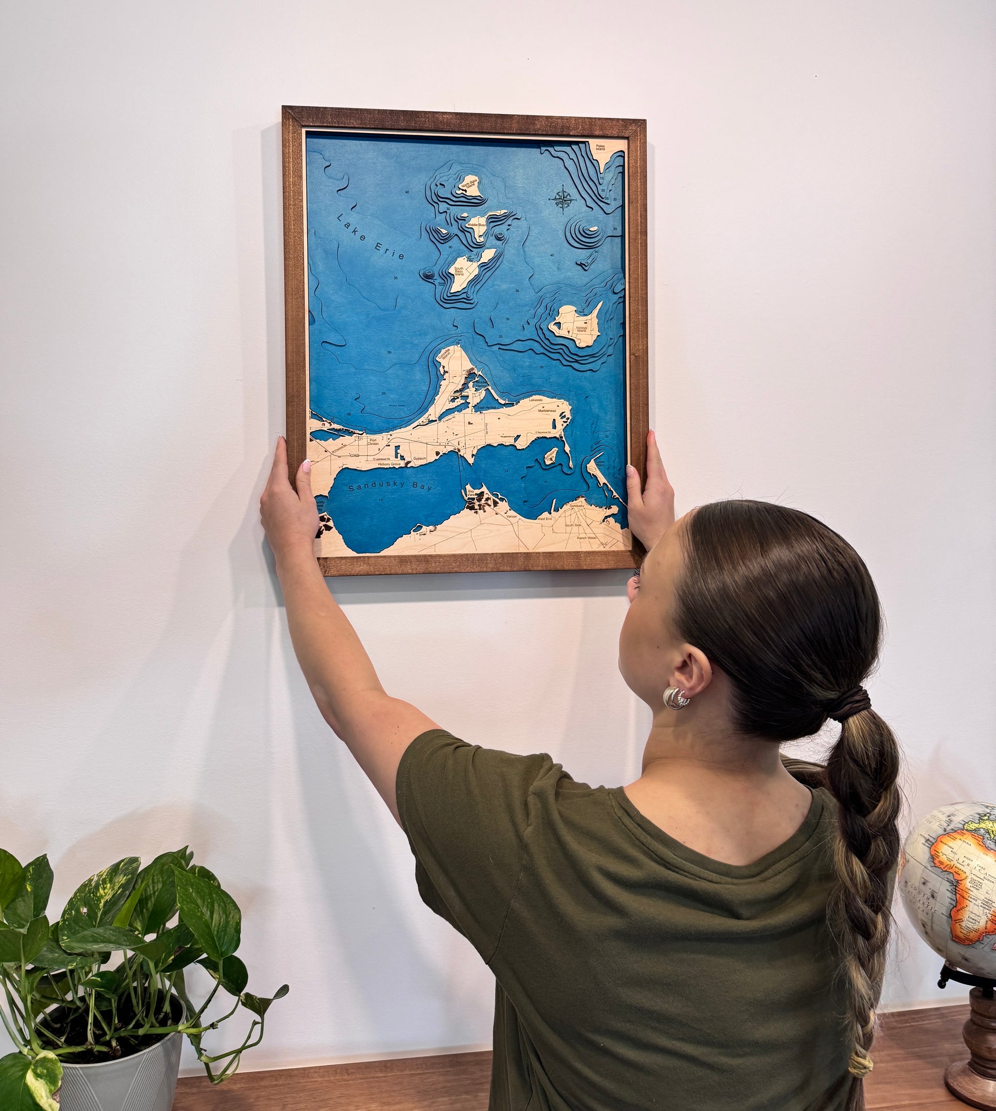 A woman hanging the Sandusky Bay Island Map on a wall.
