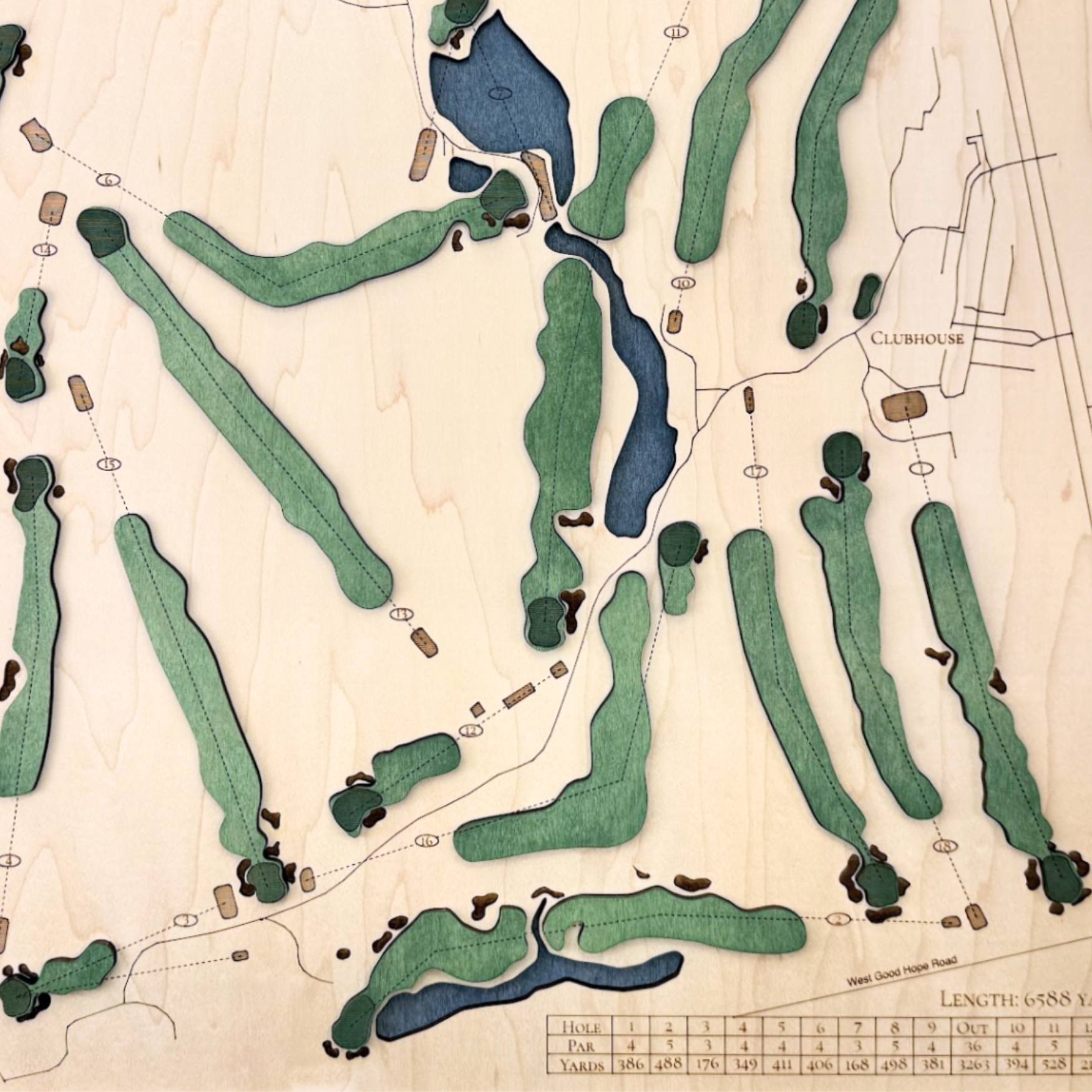 Close up of wooden golf course map with green fairways, blue water hazards, and engraved text. 