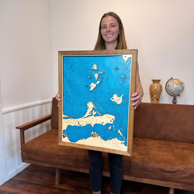 Woman holding a map of a Lake Erie Islands map with a couch and decorative items in the background. 