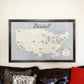 Major League baseball stadium travel map hangin on the wall above a couch. 