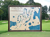 A wood golf course map pictured on a golf course green. 
