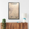 Framed custom wooden military map of Fort Benning on a wall above a wooden sideboard with decor items.
