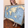 Woman holding a large framed 3D topographic world map.