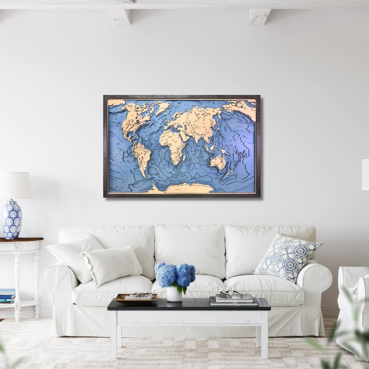 Wooden world topographic map framed on a wall above a white sofa in a living room.